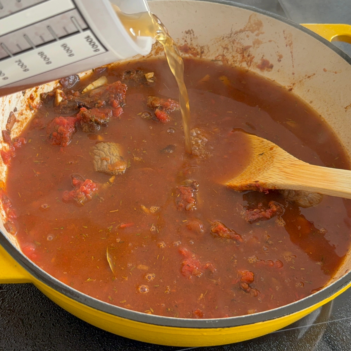 Rinderbrühe wird in den Topf gegossen, um das afrikanische Okra-Schmorgericht weiter zu kochen