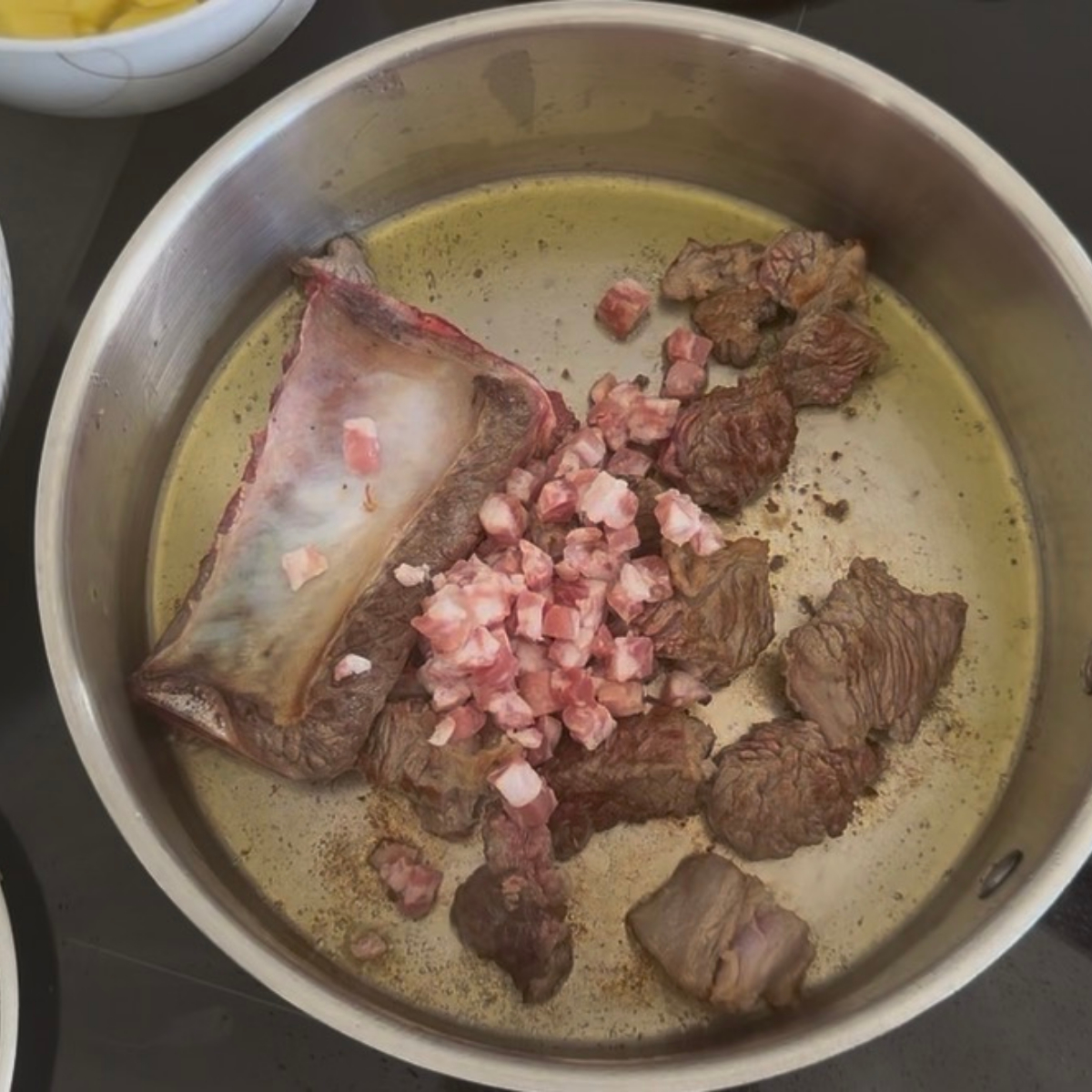 Bauchspeck wird zum angebratenen Rindfleisch in den Topf gegeben.