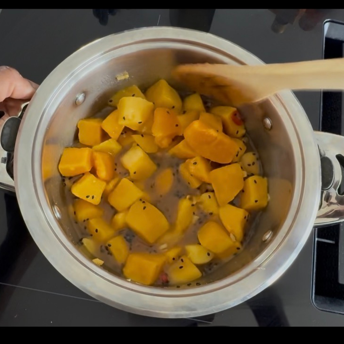 Aufgetaute Mangostücke werden zu der Gewürzmischung im Topf gegeben, um Mango-Chutney zuzubereiten.