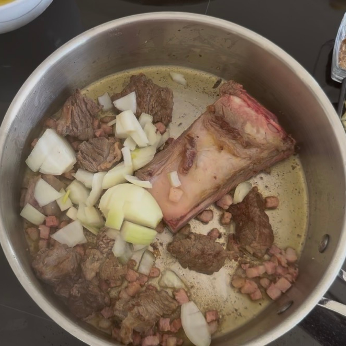 Gew&uuml;rfelte Zwiebeln werden zum angebratenen Rindfleisch und Bauchspeck in den Topf gegeben.