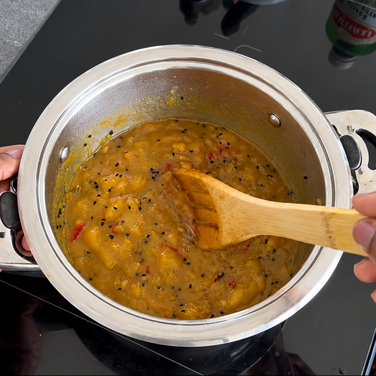 Gekochtes Mango-Chutney wird mit einem Kochlöffel leicht zerdrückt, um die gewünschte Konsistenz zu erreichen.