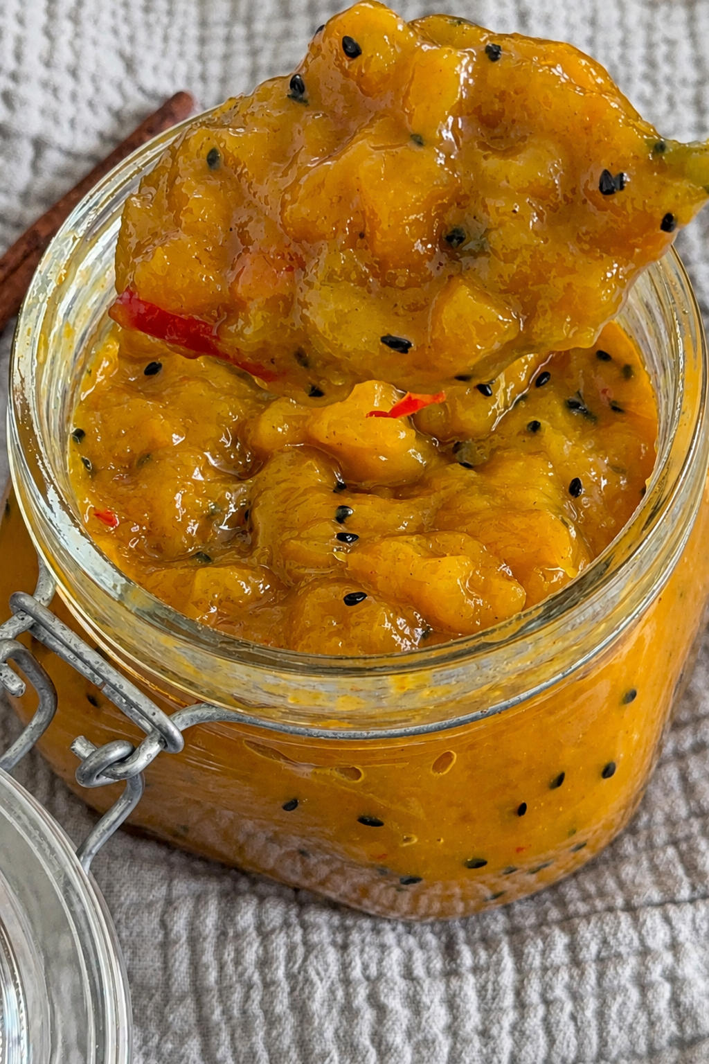 Fertiges, goldgelbes Mango-Chutney mit fruchtigen Mangostücken und Gewürzen appetitlich in einem Glas angerichtet.